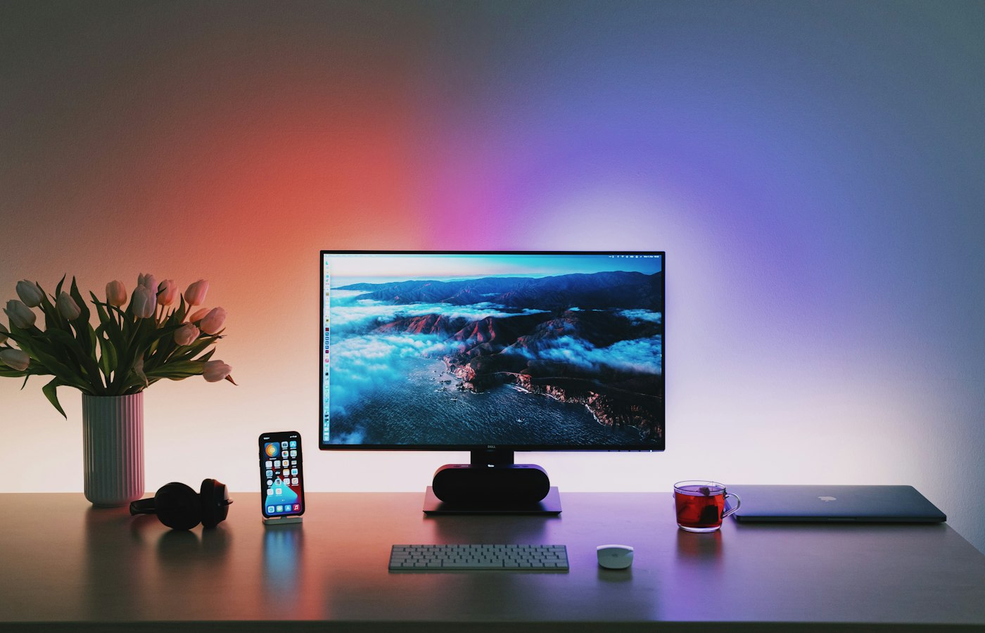 A desktop monitor glowing on a dark desk lit by coloured ambient lighting