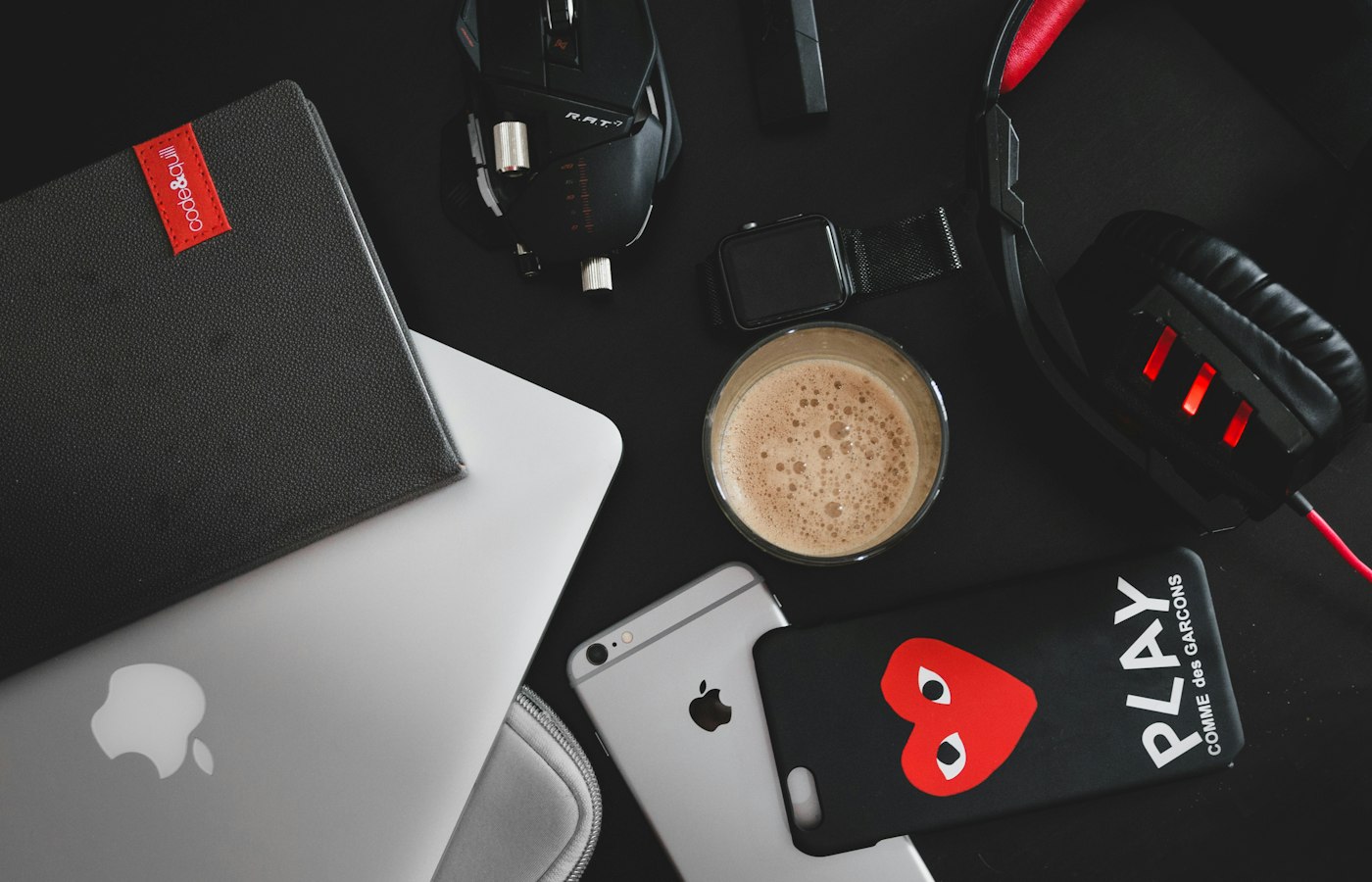 Overhead flat lay of a laptop, phone, headphones and notebook on a dark surface
